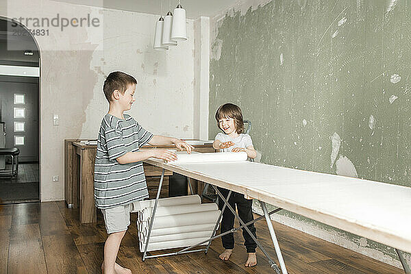 Happy brothers rolling out wallpaper on construction table at home