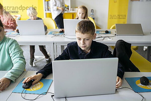 Engagierter Junge benutzt Laptop und lernt Computerprogrammierung am Schreibtisch im Klassenzimmer