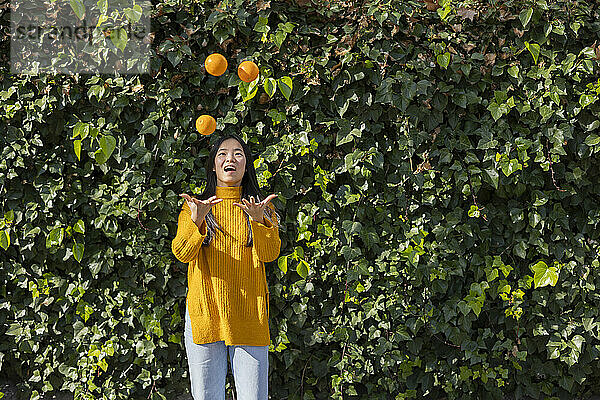 Glückliche junge Frau jongliert mit Orangen vor Pflanzen