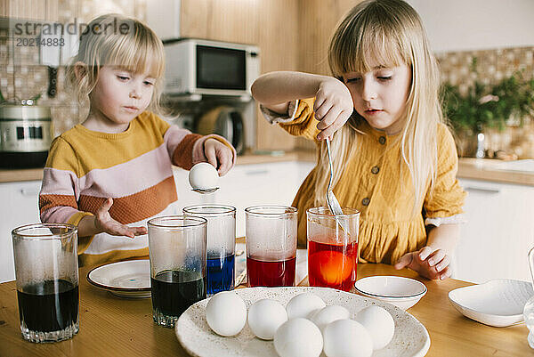 Schwestern tauchen zu Hause Ostereier in bunte Farbe
