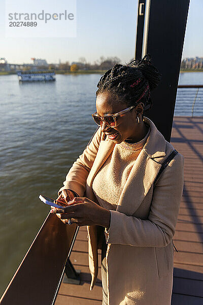 Smiling woman using smart phone near river