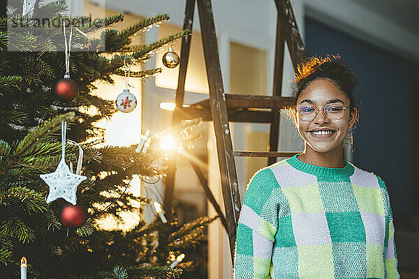Glückliche Frau im Sweatshirt  die neben dem Weihnachtsbaum steht