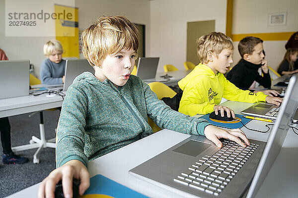 Blonder Junge benutzt Laptop und lernt am Schreibtisch Computerprogrammierung