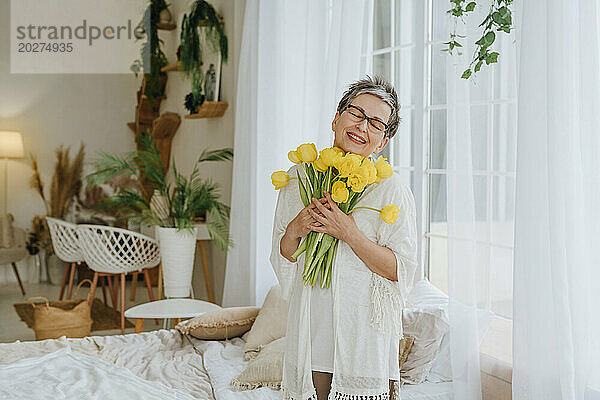 Happy woman holding bunch of tulips near window at home