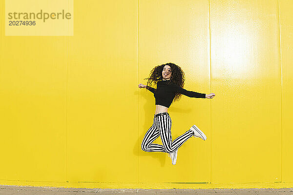 Fröhliche Frau springt in der Nähe der gelben Wand