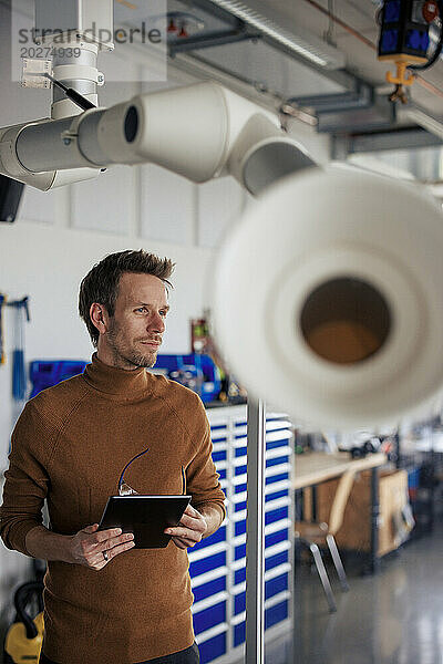 Reifer Ingenieur hält Tablet-PC in der Hand und steht in der Nähe des Absaugarms in der Werkstatt