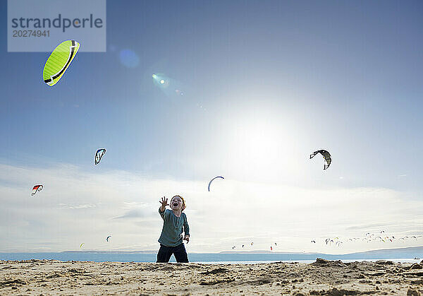 Cheerful boy watching kite surfers at beach on sunny day