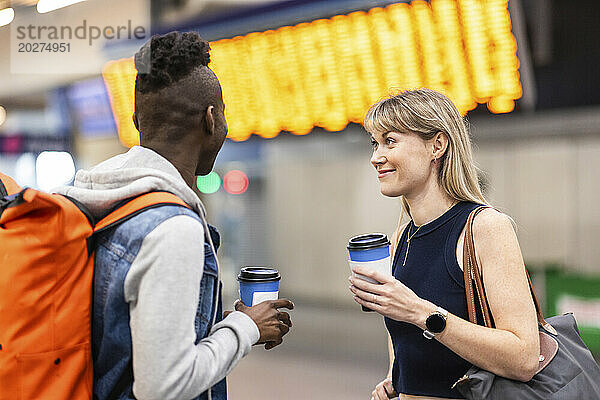Lächelnde Frau mit Freundin steht am Bahnhof