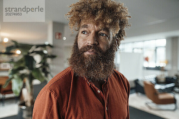 Reifer Geschäftsmann mit Bart und braunem Hemd in der Cafeteria im Büro