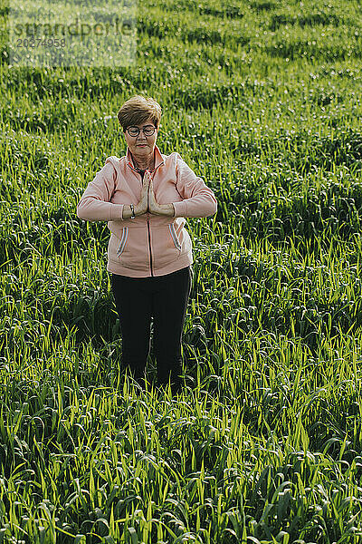 Retired senior woman practicing yoga in meadow