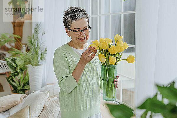 Lächelnde Frau hält zu Hause Tulpen in Vase