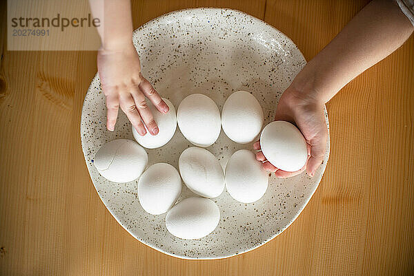 Hände von Schwestern halten Ostereier im Teller auf dem Tisch