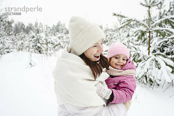 Glückliche Mutter trägt Tochter im Winterpark