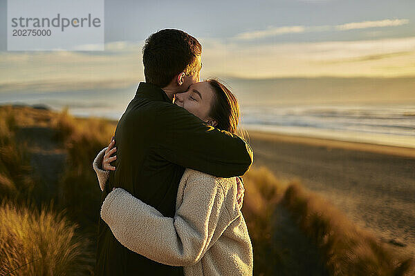 Junger Mann umarmt Freundin am Strand