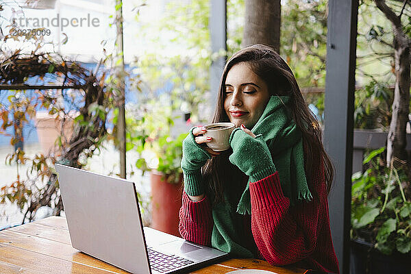 Lächelnde Frau genießt Kaffee im Café neben Laptop