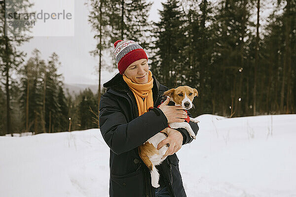 Smiling man holding pet dog in winter forest