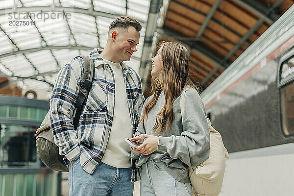 Young couple with backpacks standing at railroad station