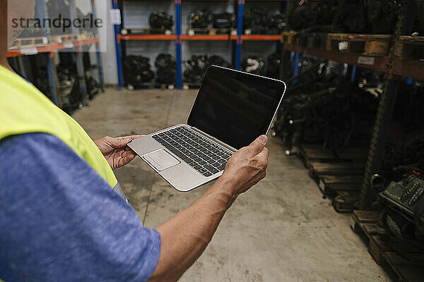 Leitender Automechaniker hält Laptop im Lager
