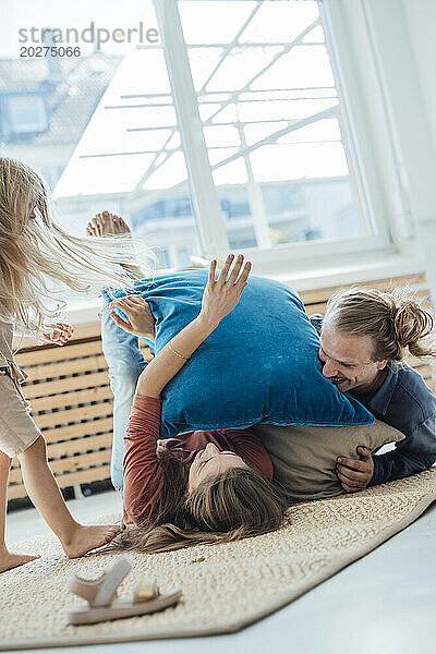 Fröhliche Familie spielt zu Hause mit Kissen auf der Matte