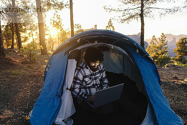 Freelancer working on laptop inside tent at sunset