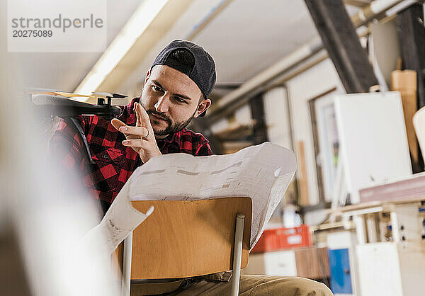 Konzentrierter Handwerker untersucht Drohne  die in der Werkstatt auf einem Stuhl sitzt