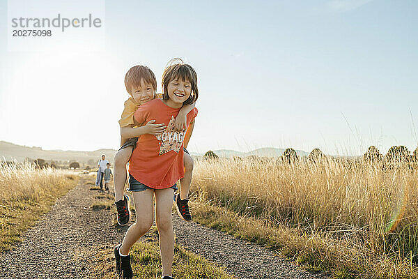 Happy sister piggybacking brother on footpath in field