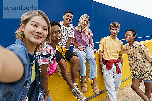 Eine Gruppe von Freunden mit farbenfroher Kleidung sitzt auf einer gelben Wand und macht ein Gruppenfoto