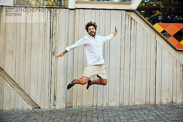 Happy young man jumping in front of wall
