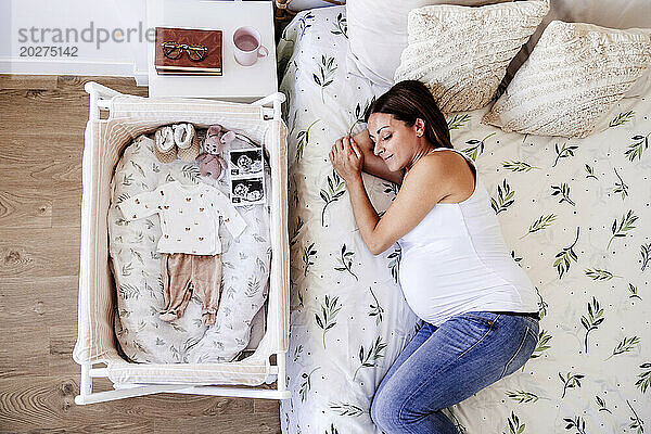 Schwangere Frau schläft zu Hause im Bett neben dem Kinderbett