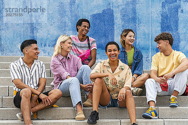 Multi ethnic group of young people sitting on steps in front of wall