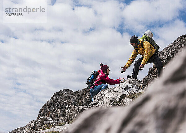 Man helping girlfriend in climbing up on mountain at Bavarian Alps  Germany