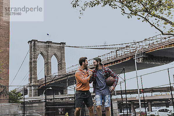 Fröhliche junge Freunde  die Spaß haben  nachdem sie in der Nähe der Brooklyn Bridge in der Stadt Basketball gespielt haben