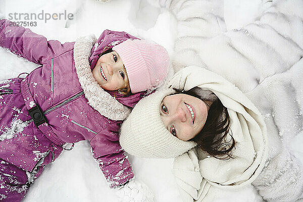 Glückliche Tochter liegt mit Mutter im Schnee