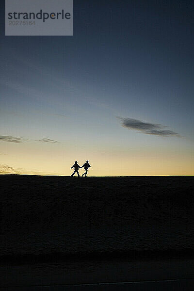Silhouette eines jungen Paares  das gemeinsam am Strand läuft