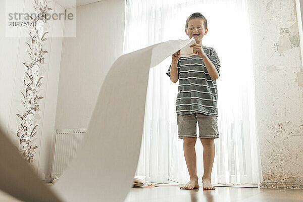 Happy boy playing with roll of wallpaper at home