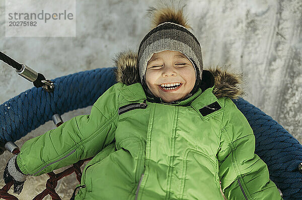 Carefree boy lying down on swing in winter at park