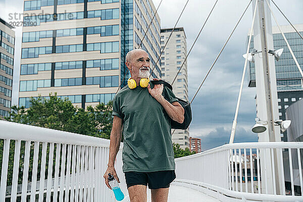 Aktiver älterer Mann läuft mit Energy-Drink-Flasche und Tasche auf der Fußgängerbrücke