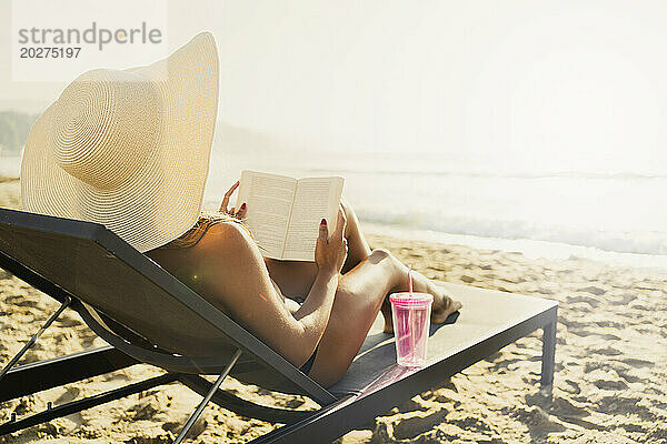 Frau liegt im Liegestuhl und liest ein Buch am Strand