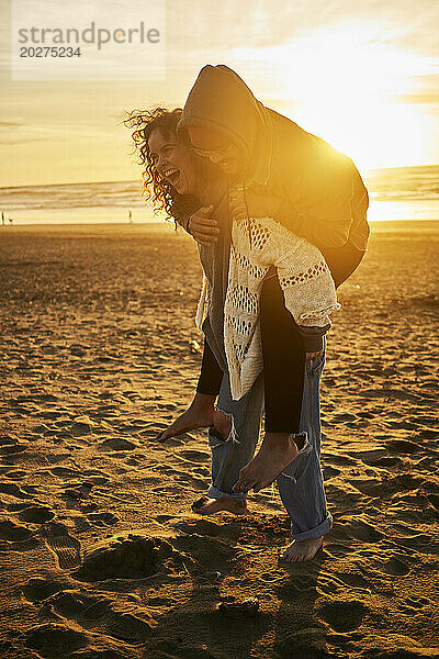 Fröhliche Frau gibt Mann am Strand Huckepackfahrt