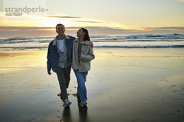 Smiling man walking with girlfriend on ocean beach