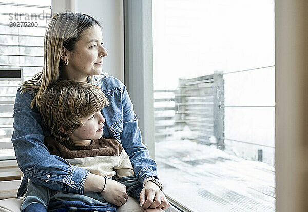 Lächelnde Mutter und Sohn schauen zu Hause durch das Fenster