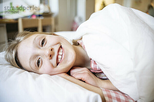 Lächelndes Mädchen  das sich zu Hause auf ein Kissen im Bett legt