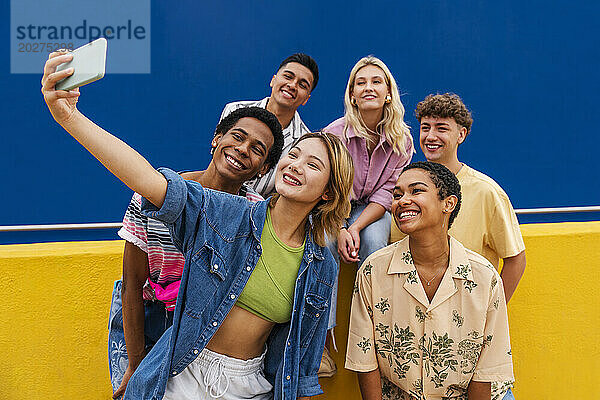 Eine Gruppe von Freunden mit farbenfroher Kleidung sitzt auf einer gelben Wand und macht ein Gruppenfoto