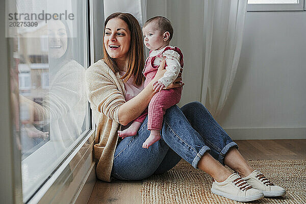 Glückliche Mutter mit Tochter  die zu Hause aus dem Fenster schaut