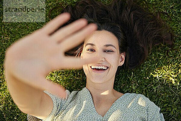 Happy woman showing stop gesture and lying on grass
