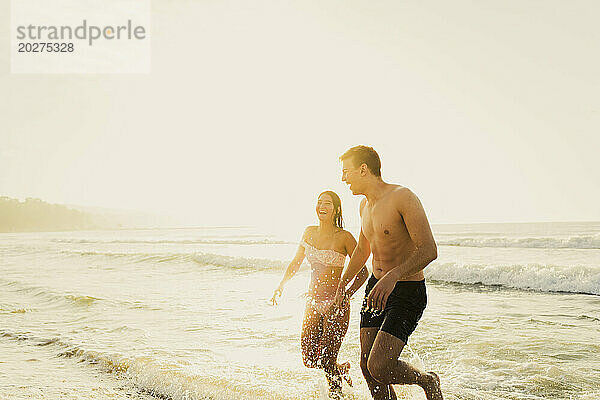 Fröhliches junges Paar spielt am Strand im Wasser