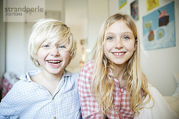 Glückliche blonde Geschwister im Pyjama zu Hause