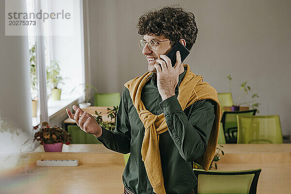 Glücklicher Geschäftsmann  der im Büro auf dem Smartphone spricht