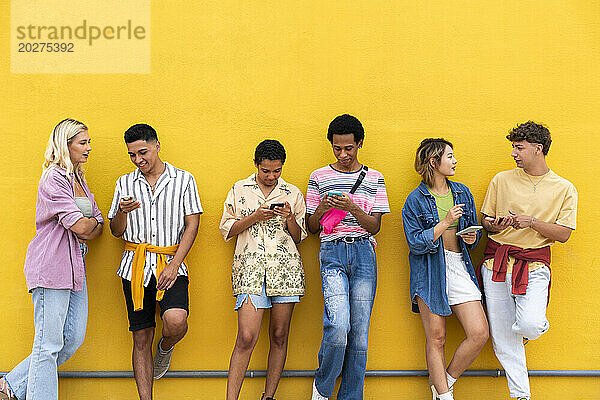 Eine Gruppe von Freunden lehnt mit ihren Smartphones an einer gelben Wand
