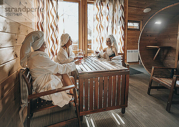 Frauen halten Weingläser in der Hand und sitzen am Tisch in der Sauna
